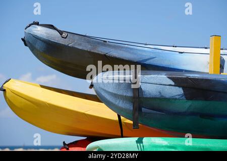 Bunte Plastikboote stapeln sich am Strand. Mehrfarbige Kanus und Kajaks auf Regalen Stockfoto