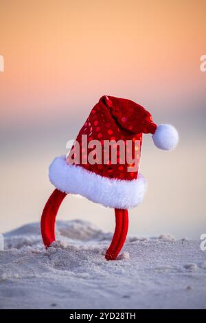 Glitzerndes rotes weihnachtsmannshut-Stirnband am Strand im frühen Morgenlicht des Sommers Stockfoto