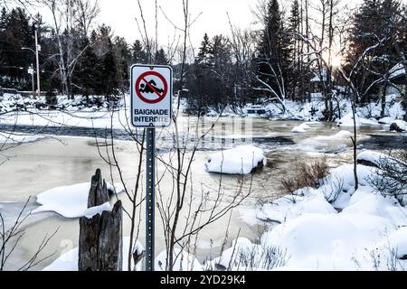 Baden verboten Schild vor einem teilweise gefroren, schnell fließenden Fluss Stockfoto