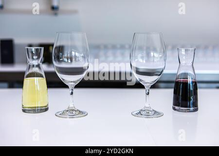 Zwei leere Weingläser und ein paar kleine Dekanter mit weißen und roten Weine gefüllt, Geschmack stemware auf einem hellen weißen Theke der Verkostungsraum Stockfoto