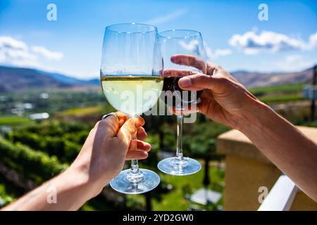 Glückliches Paar Hände zujubeln, Rot- und Weißwein Gläser von einem Weingut Weinprobe Zimmer Terrasse gegen grünen Weinbergen Landschaft, Okanagan Valley BC Kanada Stockfoto