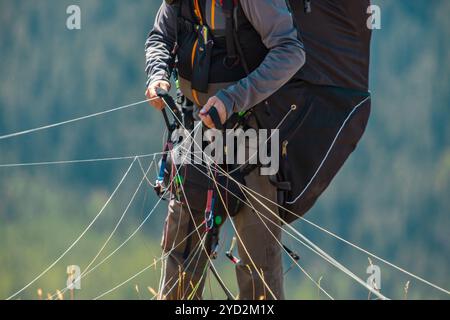 Extremaler Luftsport - Gleitschirmfliegen in Aktion. Unerkennbarer Mann, der seinen Fallschirm vorbereitet. Gleitschirmflieger bereiten sich auf den Start vor Stockfoto