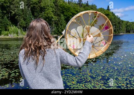 Frau, die heilige Trommel mit Stock am See spielt Stockfoto