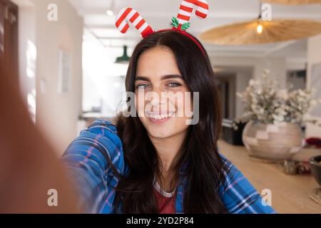 Lächelnde Frau mit festlichem Stirnband, die zu Hause Selfie macht Stockfoto