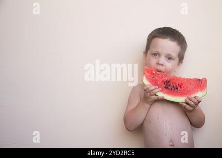 Porträt eines Jungen mit Wassermelone. Ein glückliches Kind isst eine Wassermelone. Sommer. Ein Junge an einer festen Wand mit einer Wassermelone in h Stockfoto