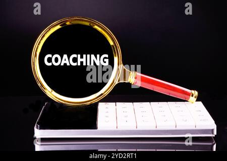 Geschäftskonzept. Das COACHING von Phrasen, Text und Wörtern wird auf schwarzem Hintergrund durch eine Lupe auf einem weißen Rechner geschrieben. Stockfoto