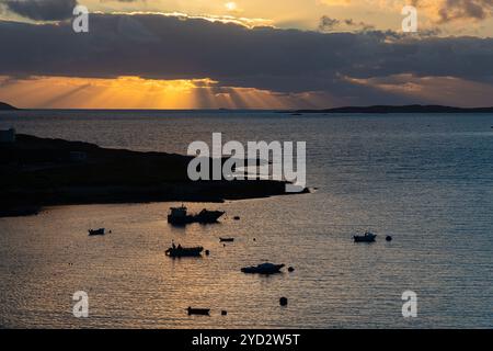 Eine Bucht in den Äußeren Hebriden (Schottland) während eines goldenen Abendhimmels, wo die untergehende Sonne spektakuläre Strahlen durch die Wolkendecke wirft. Stockfoto
