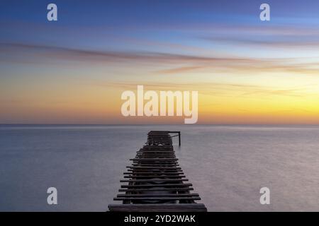 Friedliche Meereslandschaft bei Sonnenaufgang mit einem alten hölzernen Dock, der in das ruhige Meer führt Stockfoto