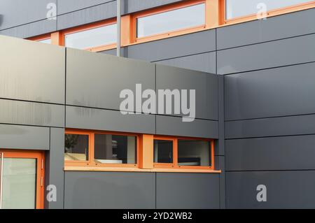Die Außenwand eines modernen Bürogebäudes mit grauer Verkleidung und orangefarbenen Fensterrahmen Stockfoto