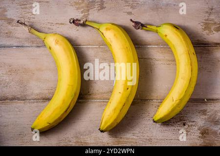 Drei ungeschälte Bananen liegen auf einem Holztisch, Blick von oben Stockfoto