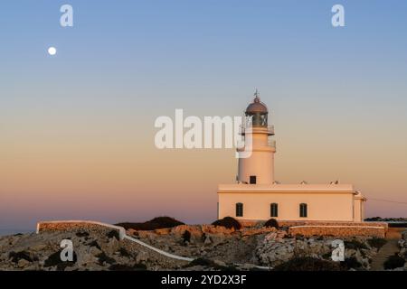 Ein vertikaler Blick auf den Leuchtturm von Cap de Cavalleria auf Menorca bei Sonnenuntergang bei aufsteigendem Vollmond Stockfoto