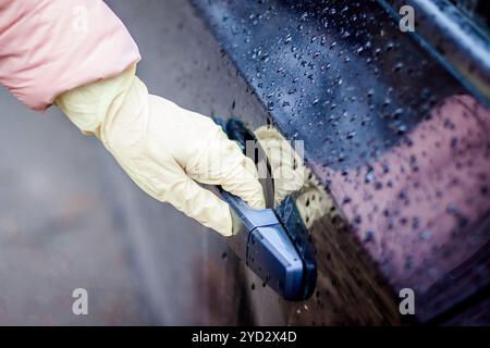 Die Hand einer Frau in einem medizinischen Handschuh öffnet die Autotür. Öffnen der Tür in medizinischen Handschuhen. Saubere Hände. Schutz vor Bakterii Stockfoto