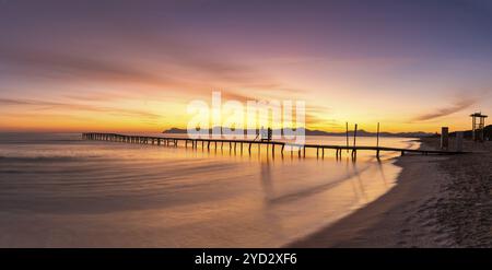 Friedliche Meereslandschaft bei Sonnenaufgang mit einem alten hölzernen Dock, der in das ruhige Meer der Alcudia Bay führt Stockfoto