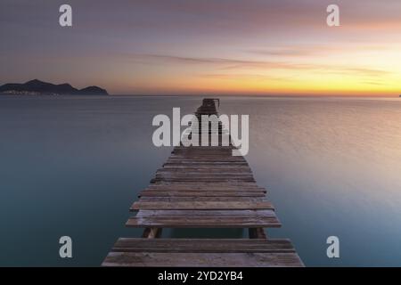 Friedliche Meereslandschaft bei Sonnenaufgang mit einem alten hölzernen Dock, der in das ruhige Meer führt Stockfoto