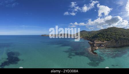 Aus der Vogelperspektive die grüne und zerklüftete hügelige Küste von Nord-Ibiza mit dem türkisfarbenen Wasser der Bucht Cala Xarraca Stockfoto