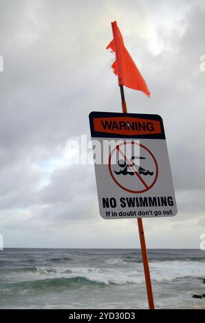 Ein Warnschild, dass man nicht schwimmen kann, neben einem stürmischen Strand Stockfoto