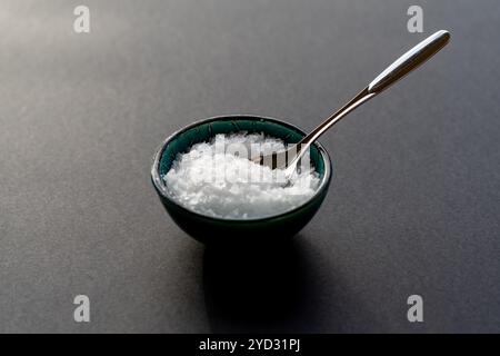 Weißes Flockensalz in einem Porzellanbecher vor schwarzem Hintergrund Stockfoto