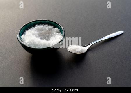 Weißes Flockensalz in einem Porzellanbecher vor schwarzem Hintergrund Stockfoto