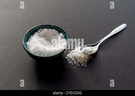 Weißes Flockensalz in einem Porzellanbecher vor schwarzem Hintergrund Stockfoto