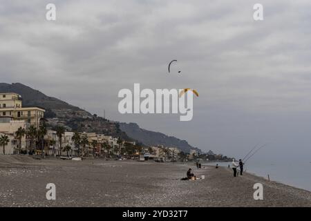 Letojanni, Italien, 29. Januar 2023: Fischer am Strand von Letojanni mit Gleitschirmfliegern, die nach einem Flug vom sizilianischen Berg hinter ihnen landen Stockfoto