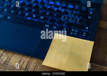 Eine gelbe Haftnotiz befindet sich auf der Unterseite einer Laptop-Tastatur. Die Notiz kann eine Erinnerung, eine Aufgabenliste oder eine Nachricht an den Benutzer sein Stockfoto