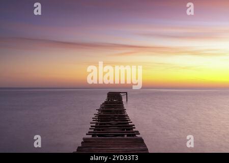 Friedliche Meereslandschaft bei Sonnenaufgang mit einem alten hölzernen Dock, der in das ruhige Meer führt Stockfoto