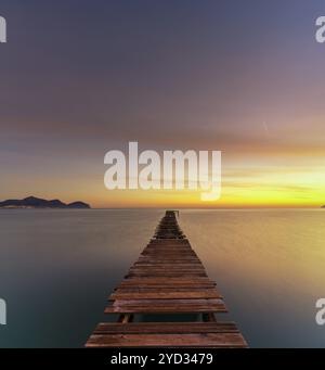 Friedliche Meereslandschaft bei Sonnenaufgang mit einem alten hölzernen Dock, der in das ruhige Meer führt Stockfoto