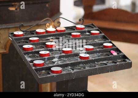 Votivstand in einer Kirche, gefüllt mit kleinen roten Kerzen Stockfoto