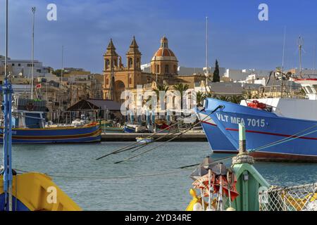 Marsaxlokk, Malta, 22. Dezember 2023: Blick auf die Innenstadt von Marsaxlokk mit der Kirche und farbenfrohen Fischerbooten im Vordergrund, Europa Stockfoto