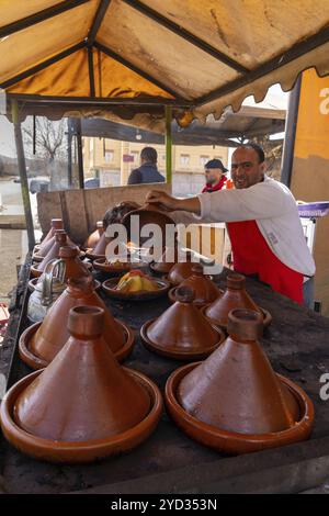 Timahdite, Marokko, 6. März 2024: Stolzer marokkanischer Koch, der seine Mahlzeiten von Tagine in seinem Straßenkochladen in Timahdite, Afrika, vorstellt Stockfoto