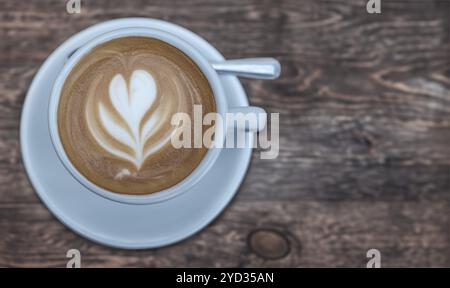 Eine Tasse Kaffee, komplett mit Latte Art in der aufschäumenden Milch, auf Einem rustikalen Kaffeetisch mit Kopierraum Stockfoto