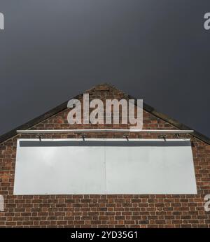 Leeres Plakatschild auf einem alten Gebäude aus roten Ziegeln mit Moody Sky Stockfoto