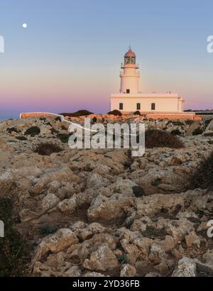 Ein vertikaler Blick auf den Leuchtturm von Cap de Cavalleria auf Menorca bei Sonnenuntergang bei aufsteigendem Vollmond Stockfoto