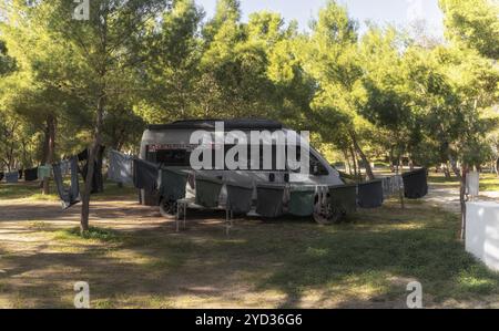 Ein grauer Wohnmobil parkt auf einem Campingplatz, umgeben von Bäumen und Kleidung, die an einer Wäscheleine im Vordergrund hängen Stockfoto