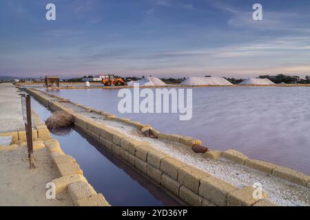 Paceco, Italien, 3. Januar 2024: Ruhige Meersalzbecken und -Ebenen bei Trapani und Paceco bei Sonnenuntergang mit Salzhaufen und Frontlader im Hinterland Stockfoto