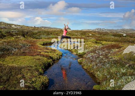 Frau läuft frei springend, kleiner mäandernder Bach im Hochland Stockfoto