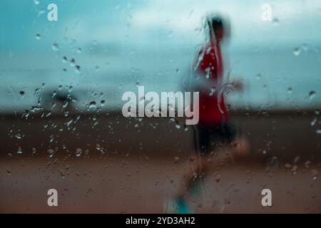 Solitary Runner durch eine verregnete Fensterscheibe auf einem Küstenlauf. Stockfoto