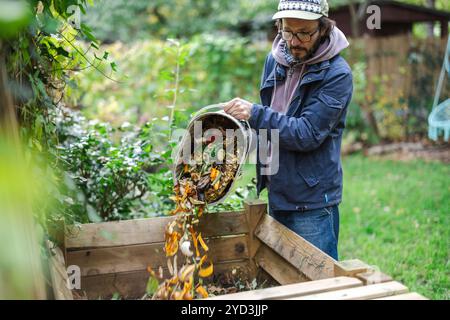 Ein Mann wirft Gemüsereste in einen Kompostbehälter im Garten Stockfoto