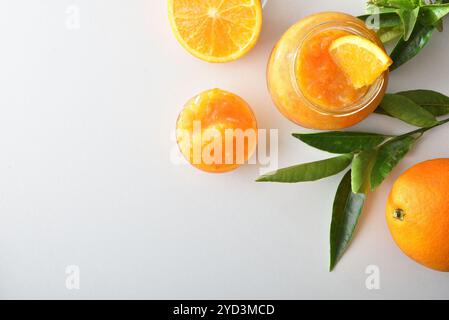 Gläser mit Orangenmarmelade auf weißem Tisch mit Früchten und Blättern. Draufsicht. Stockfoto