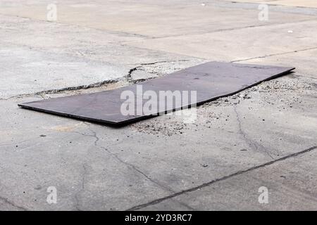 Beschädigte Betonoberfläche vorübergehende schlechte Reparatur mit dickem Eisenblech zur Abdeckung von gerissenem Zementpflaster. Stockfoto