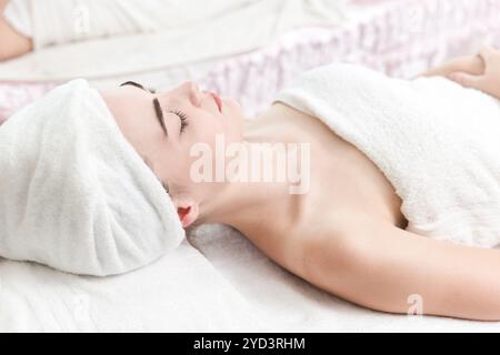 Eine junge Frau, die sich auf einem Spa-Bett mit einem Handtuch um den Kopf gewickelt hat und eine ruhige Spa-Behandlung erhält. Stockfoto