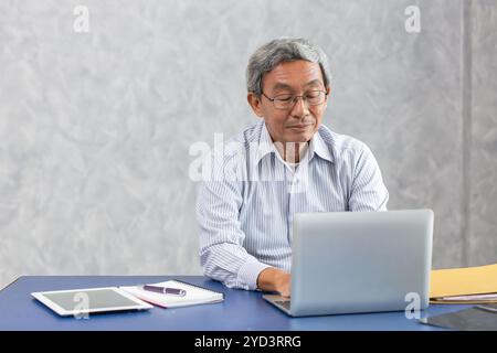 Intelligenter gesunder aktiver Senior asiatischer Geschäftsmann, der am Schreibtisch mit Laptop-Computer arbeitet Stockfoto