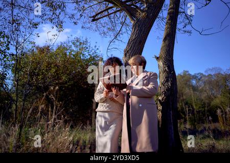 Eine Frau mittleren Alters und eine ältere Mutter mit heiliger Bibel in Händen betend für Frieden im Herbstwald Stockfoto