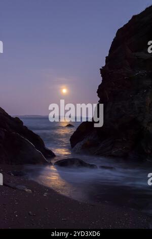 Mondaufgang durch und über Felsen am Ende des Plaidy Beach in der Nähe von Looe, Cornwall, Großbritannien, 17. September 2024, Nacht vor Super Harvest Moon, Corn Moon Stockfoto