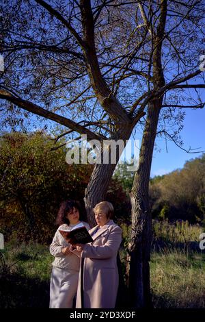 Eine Frau mittleren Alters und eine ältere Mutter mit heiliger Bibel in Händen betend für Frieden im Herbstwald Stockfoto
