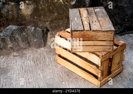 Stapel Holzkiste, der auf einem Betonboden mit Steinmauerhintergrund sitzt. Palettenkiste aus Holz. Die Kiste ist leer und aus Holz. Alt und abgenutzt Stockfoto