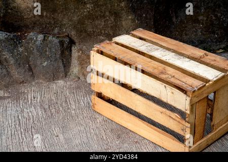 Holzkiste auf einem Betonboden mit Steinmauerhintergrund. Palettenkiste aus Holz. Die Kiste ist leer und aus Holz. Alt und abgenutzt Stockfoto