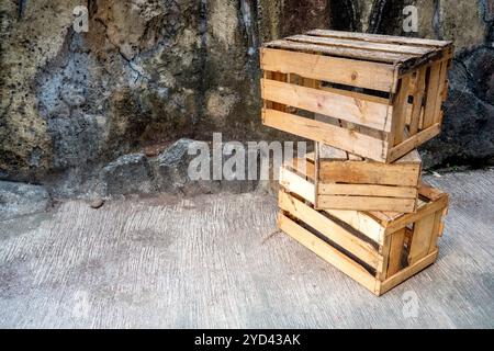 Stapel Holzkiste, der auf einem Betonboden mit Steinmauerhintergrund sitzt. Palettenkiste aus Holz. Die Kiste ist leer und aus Holz. Alt und abgenutzt Stockfoto