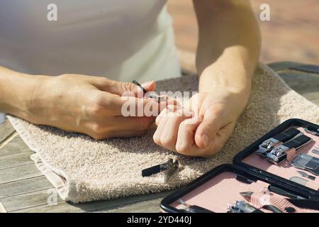 Eine Frau trimmt ihre Nägel mit einer Schere aus einem Maniküre-Set. Sparen bei Körperpflegeverfahren: Ein Mädchen macht zu Hause ihre eigene Maniküre. Stockfoto