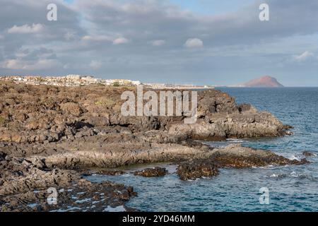 Zerklüftete Küste mit Lavasteinen nahe dem Amarilla Golf Resort in Richtung Golf del Sur und Los Abrigos Dorf und Montana Roja im Hintergrund, Teneriffa Stockfoto